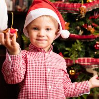 Hogyan tehetjük meghitté a karácsonyt a gyerekek számára? Christmas scene. boy gracing a christmas tree
